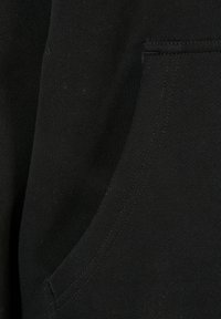 Czarna bawełniana tkanina o gładkiej fakturze, z przednią kieszenią i prostym wzorem. Szwy widoczne są wzdłuż krawędzi.