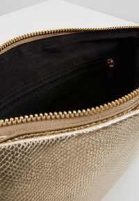 Interiér tašky se zlatým hadím vzorem, černé textilní podšívky, s výrazným zlatým zipem a kapsou na zip pro organizaci.