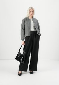 Giacca bomber grigia con colletto rotondo, top bianco, pantaloni neri larghi e una borsa in pelle nera. Tacchi a punta neri completano l'outfit.