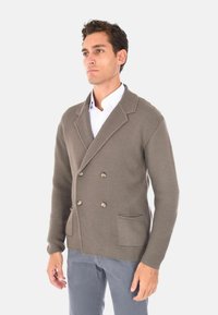 Cardigan marrone lavorato a maglia con un design doppiopetto, caratterizzato da grandi bottoni, due tasche frontali e un colletto a rever.
