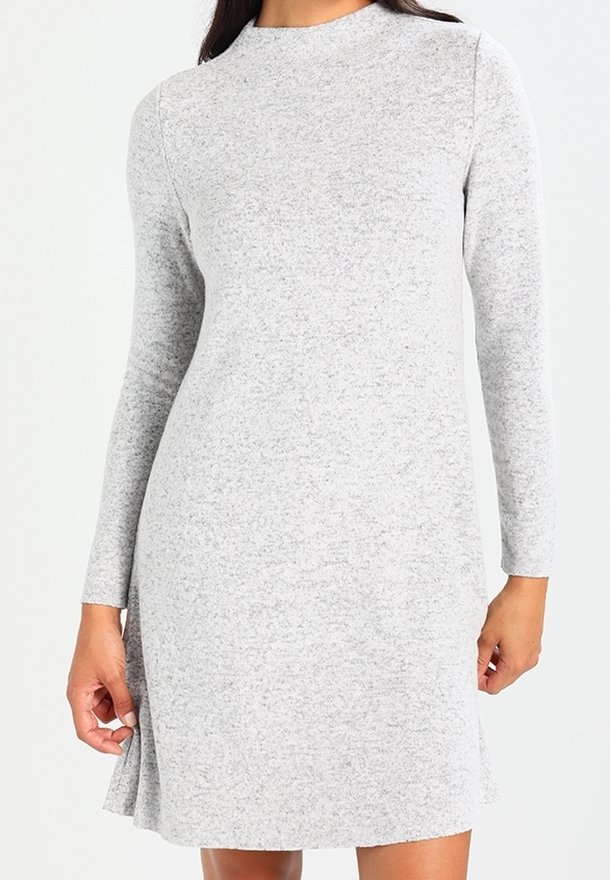 Femme portant une robe en maille gris clair à manches longues, longueur genou, avec un col montant et une texture subtile.