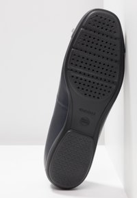 Zapato de cuero azul marino con una suela de goma texturizada que cuenta con orificios de ventilación y una parte superior lisa, marcado con "GEOX."