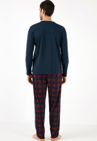 Camiseta de manga larga azul marino combinada con pantalones de pijama a cuadros en rojo y azul marino. El material parece suave; los pantalones presentan un patrón a cuadros.