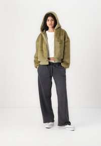 Oliivroheline faux fur bomber-jakk kapuutsiga, koos mustade laia säärtega pükste ja valgete tennisekingadega. Tekstureeritud kangas ribatud varrukatega.
