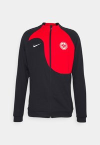 Chaqueta atlética negra y roja con cremallera frontal, mangas largas y el emblema de Frankfurt en el lado izquierdo del pecho. Logo de Nike en blanco en el lado derecho.