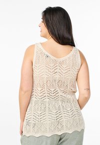 Beige, ärmelloses Strickoberteil mit einem gemusterten, offenen Gewebe und einem gewellten Saum. Der Rücken betont ein geometrisches Design und eine lockere Passform.