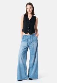 Black sleeveless vest with buttons, paired with light blue, wide-leg denim pants featuring elastic waist and front pockets.