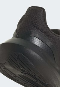 Czarne sportowe buty z teksturowanym wierzchem, gładkim zapiętkiem i wzorzystą gumową podeszwą z widocznymi rowkami antypoślizgowymi.