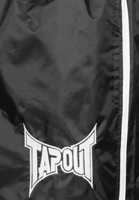 Crna jakna od sjajnog materijala s istaknutim bijelim izvezenim logom "TAPOUT" modernog dizajna i kontrastnim bijelim zatvaračem.