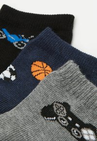 Trzy pary skarpetek: czarne z niebieskim motocyklem, granatowe z pomarańczowym koszykówką oraz szare z motywem kontrolera do gry, wszystkie o plecionym wzorze.