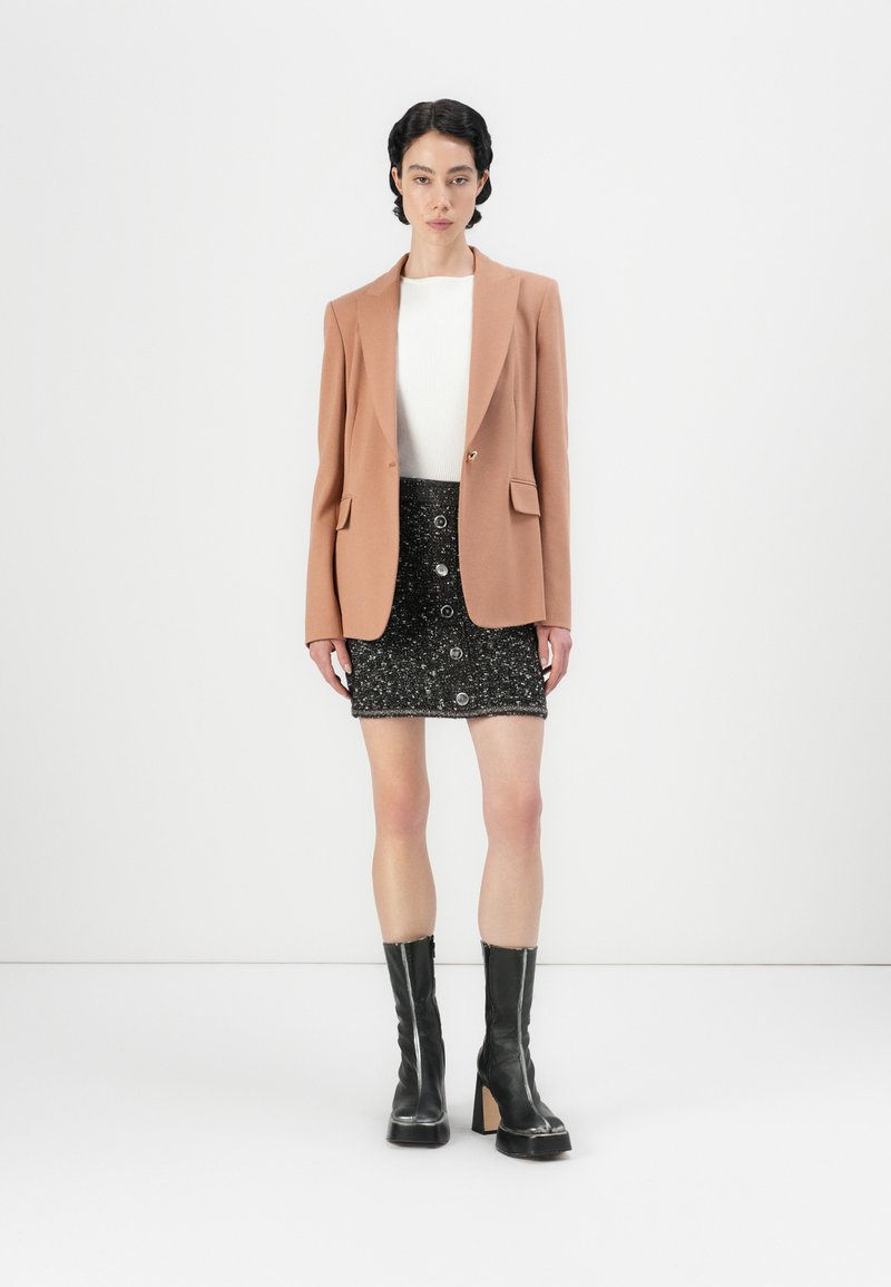 Jasnobrązowa żakietowa marynarka noszona na białej bluzce, w połączeniu z czarną błyszczącą mini spódnicą z guzikami. Czarne botki na obcasie o fakturowanej powierzchni.