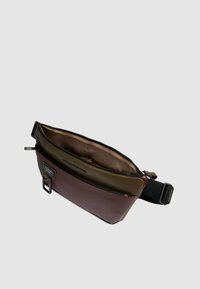 Bolsa en marrón y verde oliva con cierre de cremallera, exterior liso, correa ajustable y compartimento interior. Forma rectangular con texturas sutiles.