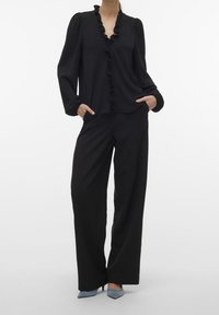 Blouse noire avec un col à volants et des manches longues, associée à un pantalon noir à jambes larges et des chaussures à talons hauts bleues. Texture lisse.