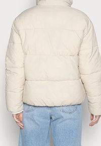 Pufjakke i lys beige med horisontale quiltede sektioner og høj krave. Kombineret med lys blå distressed denim jeans.