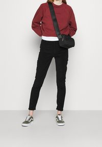 Bordådsfärgad kortärmad sweatshirt med präglad logotyp, svarta skinnybyxor, olivgröna och vita sneakers samt en liten svart crossbody-väska.