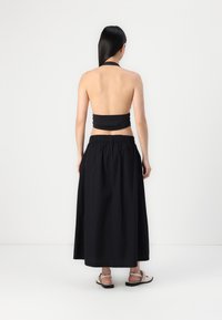 Svart halter crop top kombinert med et langt, flytende svart skjørt. Glatt stofftekstur, elastisk midje, og flate sandaler.