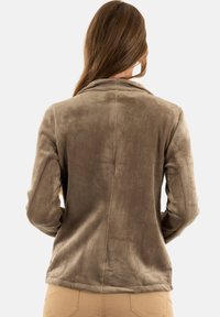 Giacca in velluto a coste marrone con una texture morbida, colletto e maniche lunghe. Presenta costine verticali e un design della schiena sartoriale.