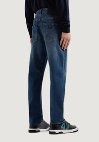 Pantalones vaqueros de mezclilla azul con un corte relajado, que cuentan con dos bolsillos traseros, un parche de marca en la cinturilla y detalles de costura en contraste.