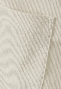 Crème-kleurige ribstof met een gestikte rechthoekige zak die een gedetailleerde textuur en zijnaadstiksels toont.