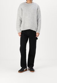 Maglione grigio a maglia con scollatura rotonda e polsini a coste, abbinato a pantaloni cargo neri con tasche laterali e sneakers nere con suola in gomma.