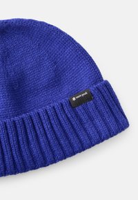 Beanie lavorato a maglia di un blu vivace, con fondo a costine e un’etichetta nera con testo bianco. Texture liscia e vestibilità aderente.