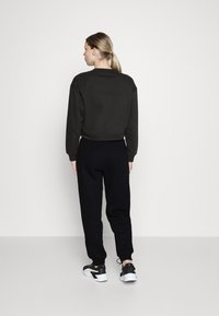 Felpa nera cropped con polsini a costine, abbinata a pantaloni jogger neri e sneakers nere con suola bianca. Tessuto dallo stile liscio.