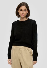 Schwarzer Strickpullover mit Rundhalsausschnitt und langen Ärmeln, kombiniert mit beigen Cargo-Hosen mit elastischem Bund und seitlichen Taschen.