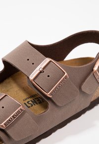 Sandelia marrón de Birkenstock con dos correas ajustables y hebillas de bronce, material sintético texturizado y plantilla de corcho.