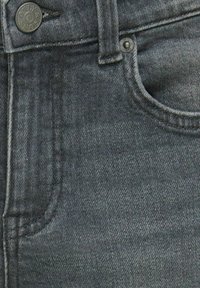 Ciemnoszary denim o gładkiej fakturze, z zapięciem na guzik i przednią kieszenią. Widoczne szwy wzdłuż szwów.