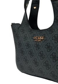 Bolso negro de Guess con patrón de logo texturizado y emblema dorado "GUESS EST 1981", que presenta una corta doble asa y detalles en tono dorado.
