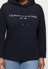 Granatowa bluza z kapturem z frontowym logo "TOMMY HILFIGER EST 1985" w białym i czerwonym kolorze, z sznurkiem ściągającym i luźnym krojem.