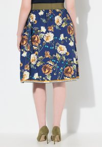 Kukkallinen hame, jossa on tummansininen tausta, auringonkukkia ja vihreitä korostuksia, kireä vyötärö ja koristeellinen reunus helmassa.