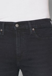 Jeans de mezclilla oscura con un diseño ajustado, que cuentan con cierre de botón y cremallera, cinco bolsillos y sutiles detalles de costura.