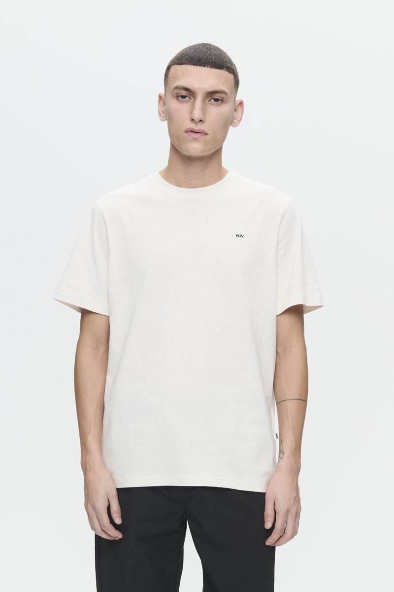 Crèmekleurig katoenen t-shirt met korte mouwen, een ronde halslijn en een klein zwart logo op de linkerborst. Eenvoudig ontwerp, ontspannen pasvorm.