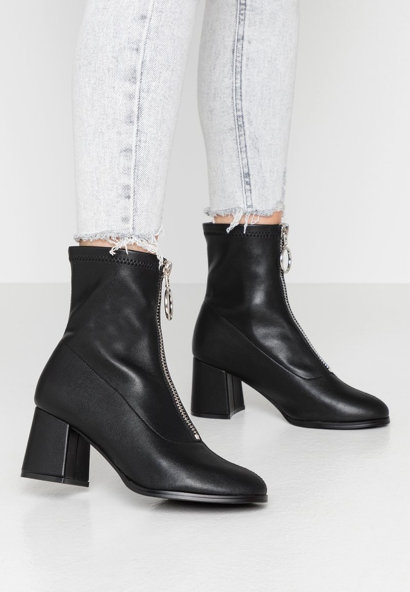 Bottines en cuir vegan noir avec fermeture éclair, talons carrés et texture lisse. Présente un design épuré avec des accents minimalistes.
