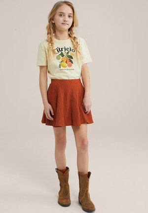 Cremefarvet grafik t-shirt med frugtdesign, parret med en tekstureret rustfarvet skater-nederdel og brune ankelstøvler.