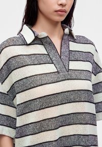 Jeune personne portant un haut en maille rayé horizontal noir et blanc avec un col court et un décolleté ouvert.