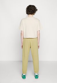 Beige cropped t-shirt paired with light green sweatpants. Pants feature elastic cuffs; model wears green and white sneakers. Plain background.