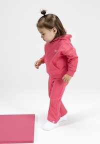 Roze hoodie en joggingset, gemaakt van zachte stof. Bevat een voorkantzak en witte sneakers. Eenvoudig ontwerp, geen patronen.