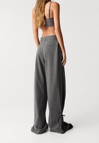 Pantalons larges en tissu gris foncé, avec une taille haute, des poches latérales et des accents à nouer au bas pour une longueur ajustable.