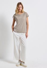 Vaaleanbeige lyhythihainen t-paita, jossa on pyöreä kaula-aukko, yhdistettynä leveisiin valkoisiin housuihin ja vaaleisiin tennareihin, luoden rennon asukokonaisuuden.