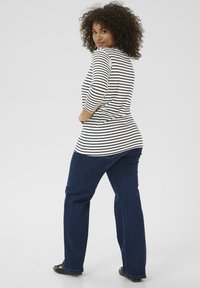 Black and white striped long-sleeve top with rounded neckline, paired with dark blue straight-leg jeans. Model stands with a slight turn.