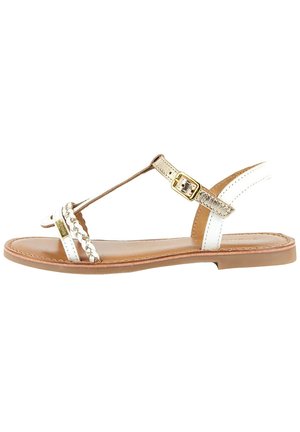 Sandalias de cuero blanco con suela plana, que cuentan con detalles trenzados y una hebilla dorada. Diseñadas con una tira en T para un ajuste seguro.