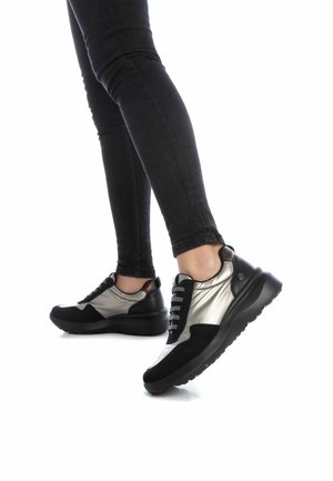 Baskets noires et argent métallisé avec un dessus texturé, bout rond, lacets noirs et semelle épaisse, portées avec un jean noir ajusté.