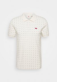 Krämfärgad pikétröja med krage, prydd med små svarta geometriska mönster och en röd Levi's-logotyp på vänster bröst. Korta ärmar och mjuk textur.