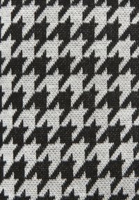 Čiernobiela houndstooth vzorovaná textília s textúrovaným tkaním, ktorá zobrazuje striedajúce sa tvary v oboch farbách v mriežkovom usporiadaní.