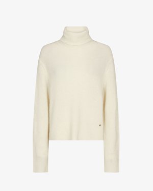 Cream-colored knit turtleneck sweater with long sleeves and ribbed cuffs, showing a small round metal logo near the hem.