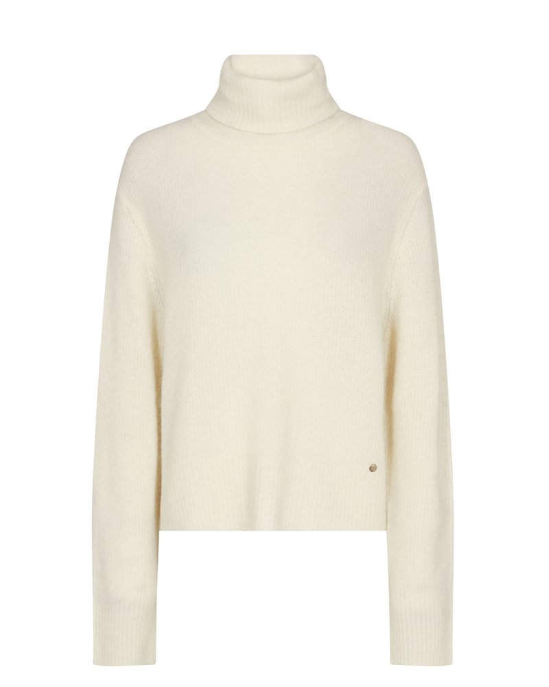 Cream-colored knit turtleneck sweater with long sleeves and ribbed cuffs, showing a small round metal logo near the hem.