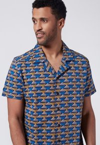 Camisa de manga corta con un patrón de olas en azul, amarillo y blanco. Confeccionada en tejido ligero, cuenta con un diseño de botonadura frontal y collar puntiagudo.