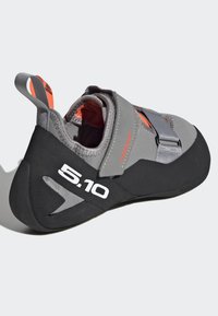 Sapatos de escalada cinzentos com detalhes em laranja, apresentando um calcanhar elástico, tiras de fecho em velcro e uma sola texturizada em borracha preta.